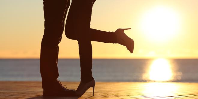 Silhouette of a couple's legs while embracing on the beach at sunset