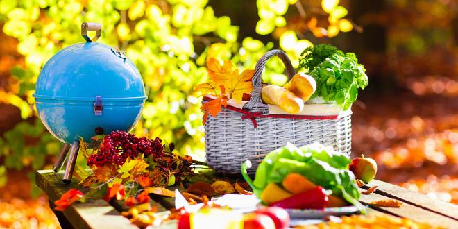 A portable grill and picnic basket on an outdoor table.