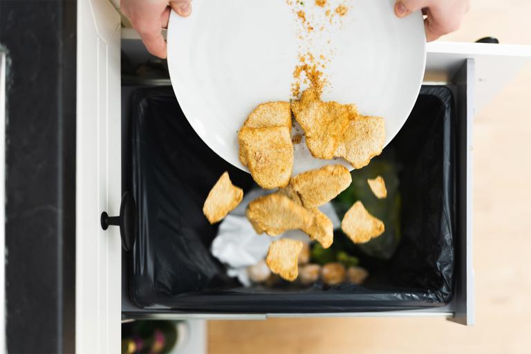 someone dumping good food into the kitchen trash